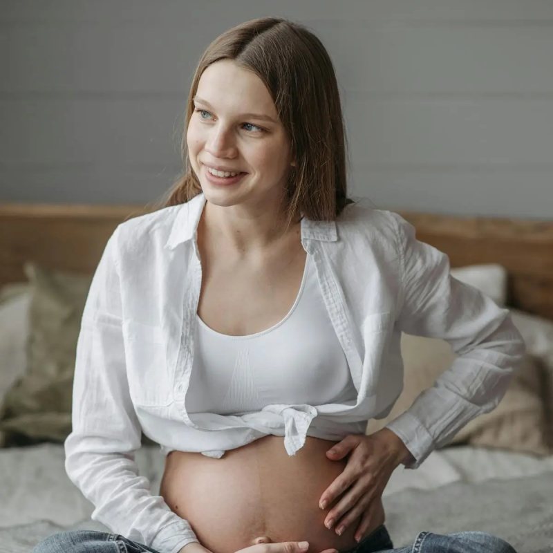 A pregnant woman smiling, sitting cross-legged at home