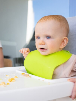 A baby sitting in a high chair with soft finger food on the tray